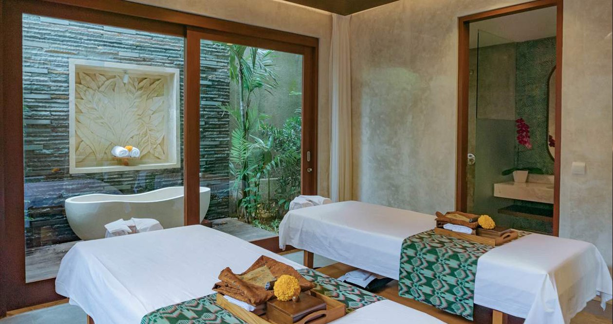 A luxury massage room in elysian day spa in F7 Islamabad with two massage beds, a bathtub, soft towels, fresh flowers, and massage oils. The room is calm and peaceful, with soft lighting and simple, relaxing decor.